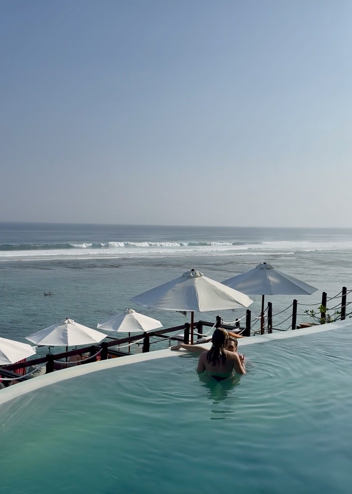 Infinity pool overlooking the ocean and white umbrellas at Kiva Beach Club, Uluwatu