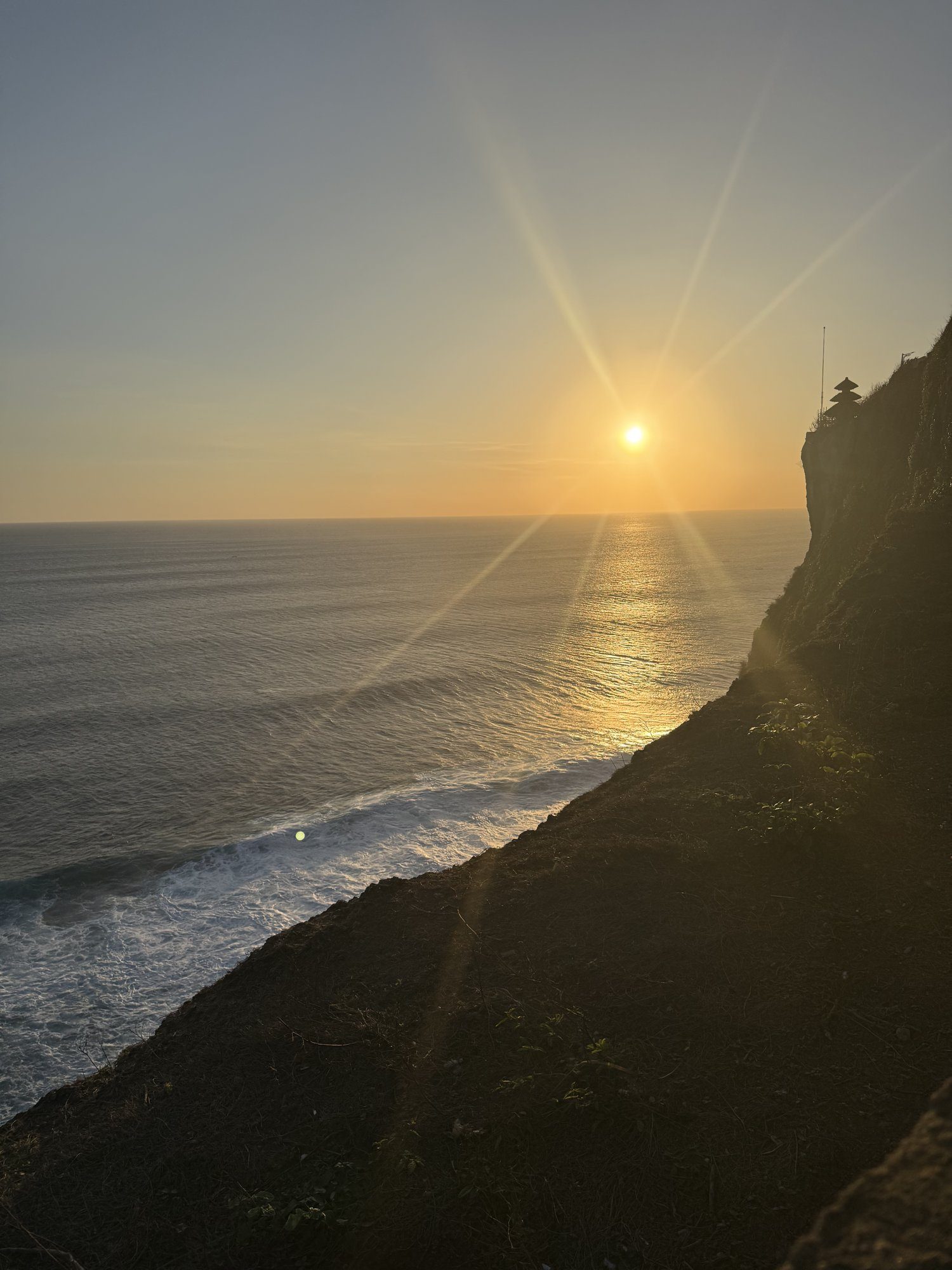 Sun setting over the ocean beside the clifftop Uluwatu Temple