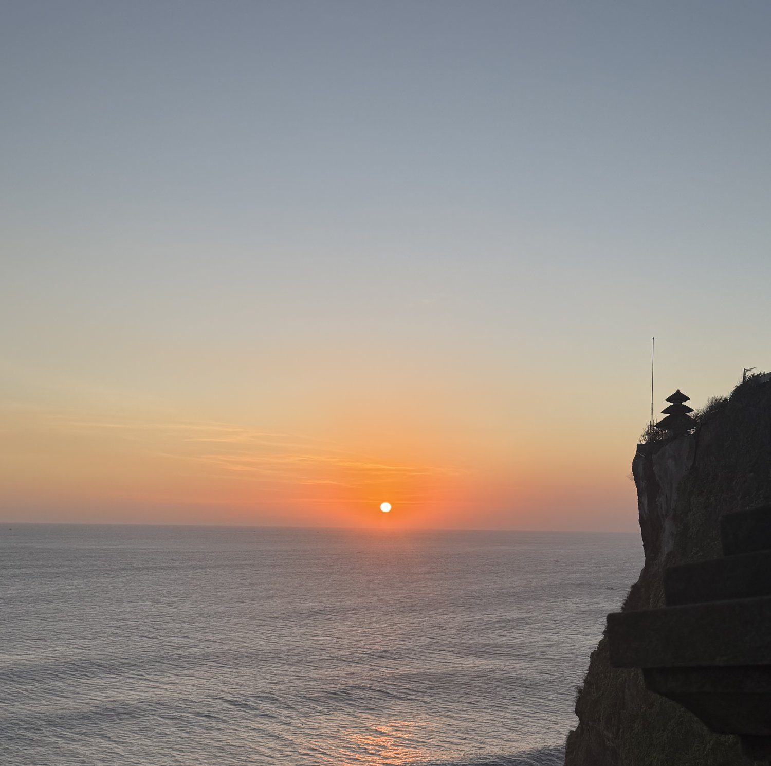 Orange sunset over the Indian Ocean with the Uluwatu Temple pagoda silhouetted on the cliff